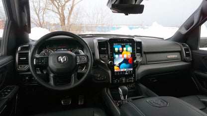 Interior of a Ram 1500 pickup showing the steering wheel and center console with the 12-inch Uconnect 5 touchscreen upgrade installed and turned on.
