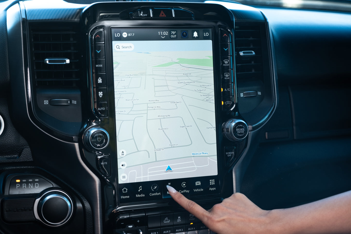 Close-up of a Ram 2500’s 12-inch Uconnect 5 screen displaying a navigation map and audio controls while a person’s finger points at the screen.
