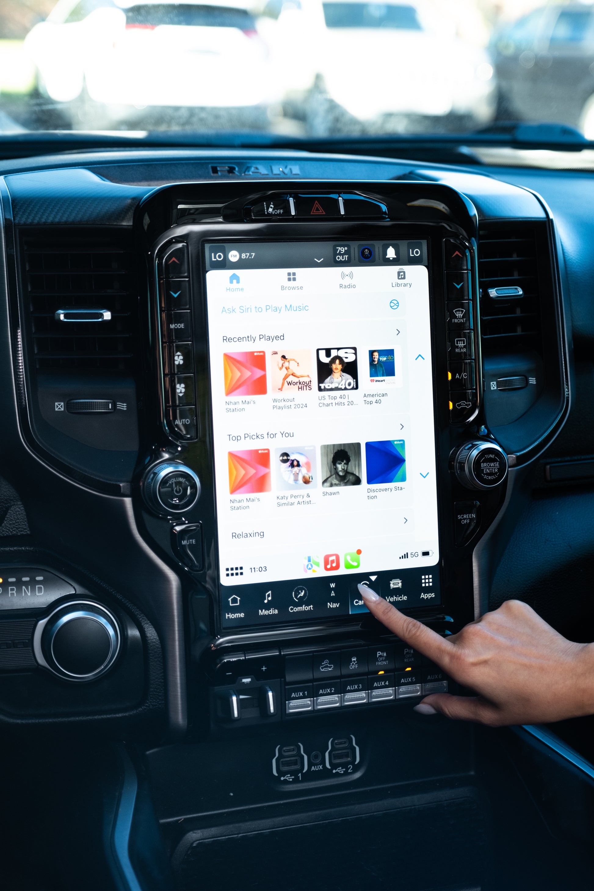 Night view inside a Ram HD truck showing the illuminated 12-inch Uconnect upgrade; a hand points at the touchscreen interface.