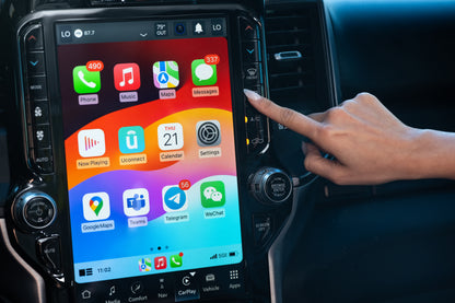 A person interacts with the large 12-inch Uconnect 5 touchscreen in a Ram truck’s dashboard, selecting an app on the Apple CarPlay interface.